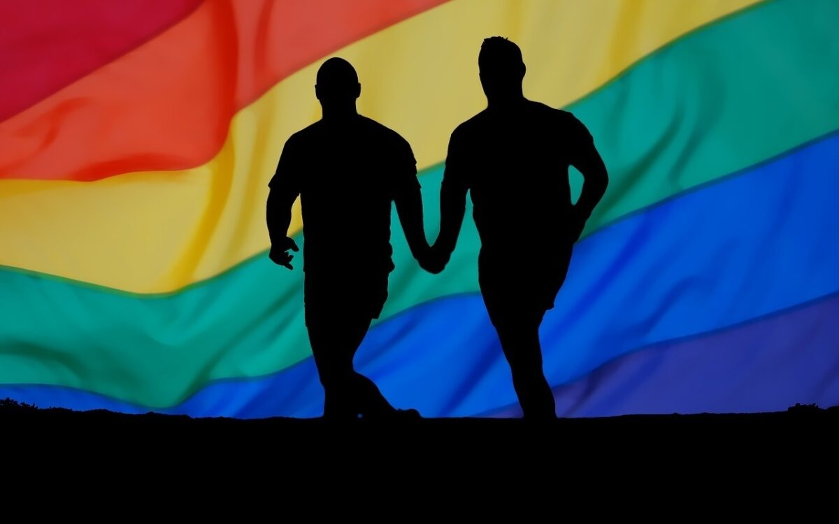 Ein Männerpaar hält die Hände im Hintergrund die Regenbogenfahne Ein Männerpaar hält die Hände im Hintergrund die Regenbogenfahne
